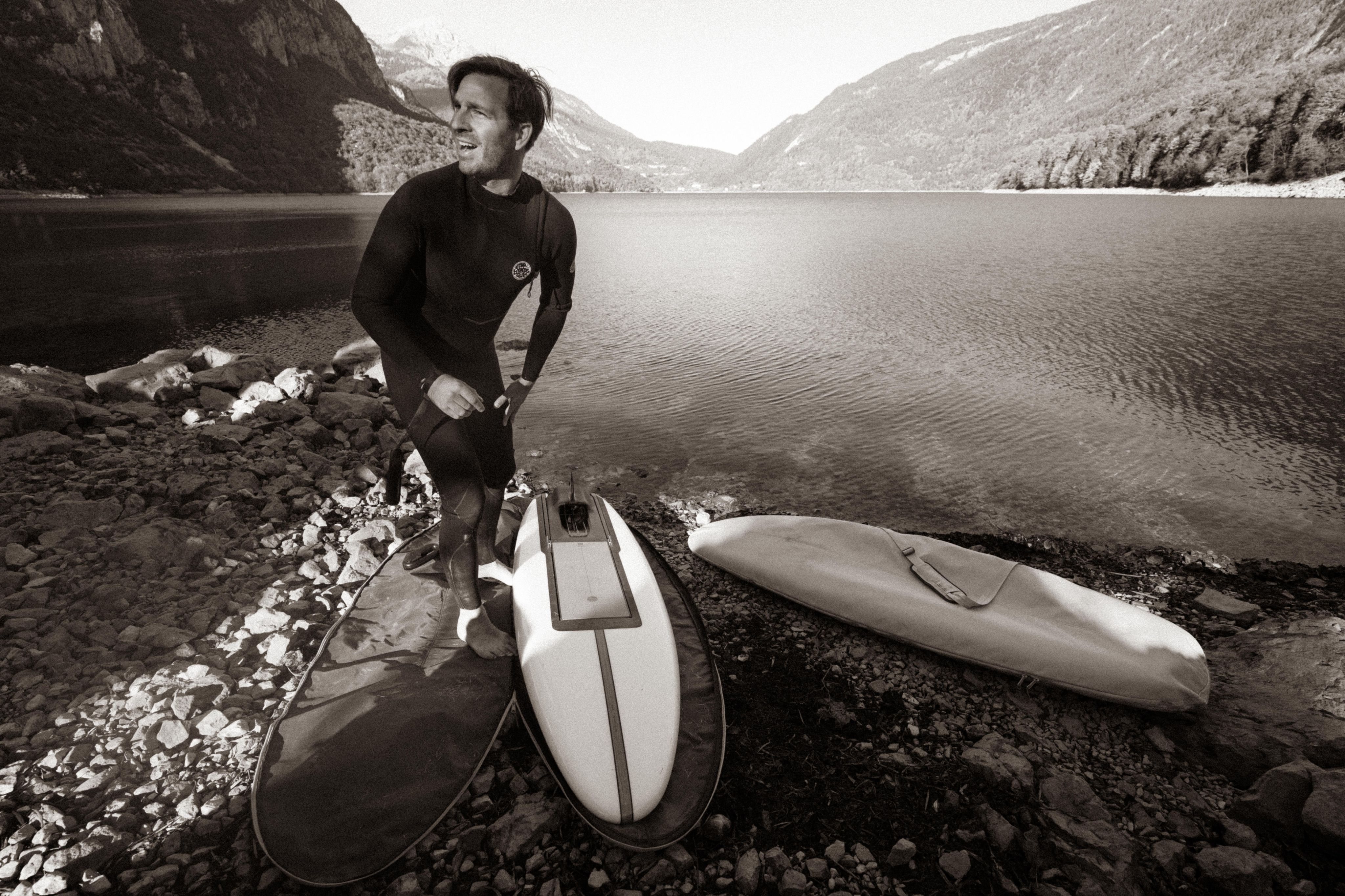Surfer in wetsuit with two LIND electric surfboards by a mountain lake