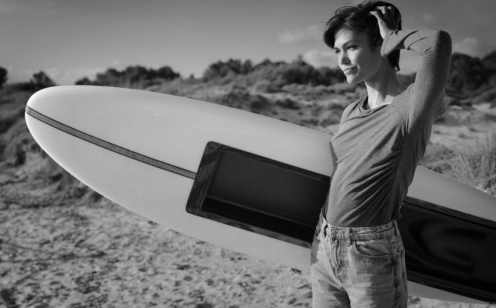 Woman posing next to a LIND electric surfboard on a sandy beach