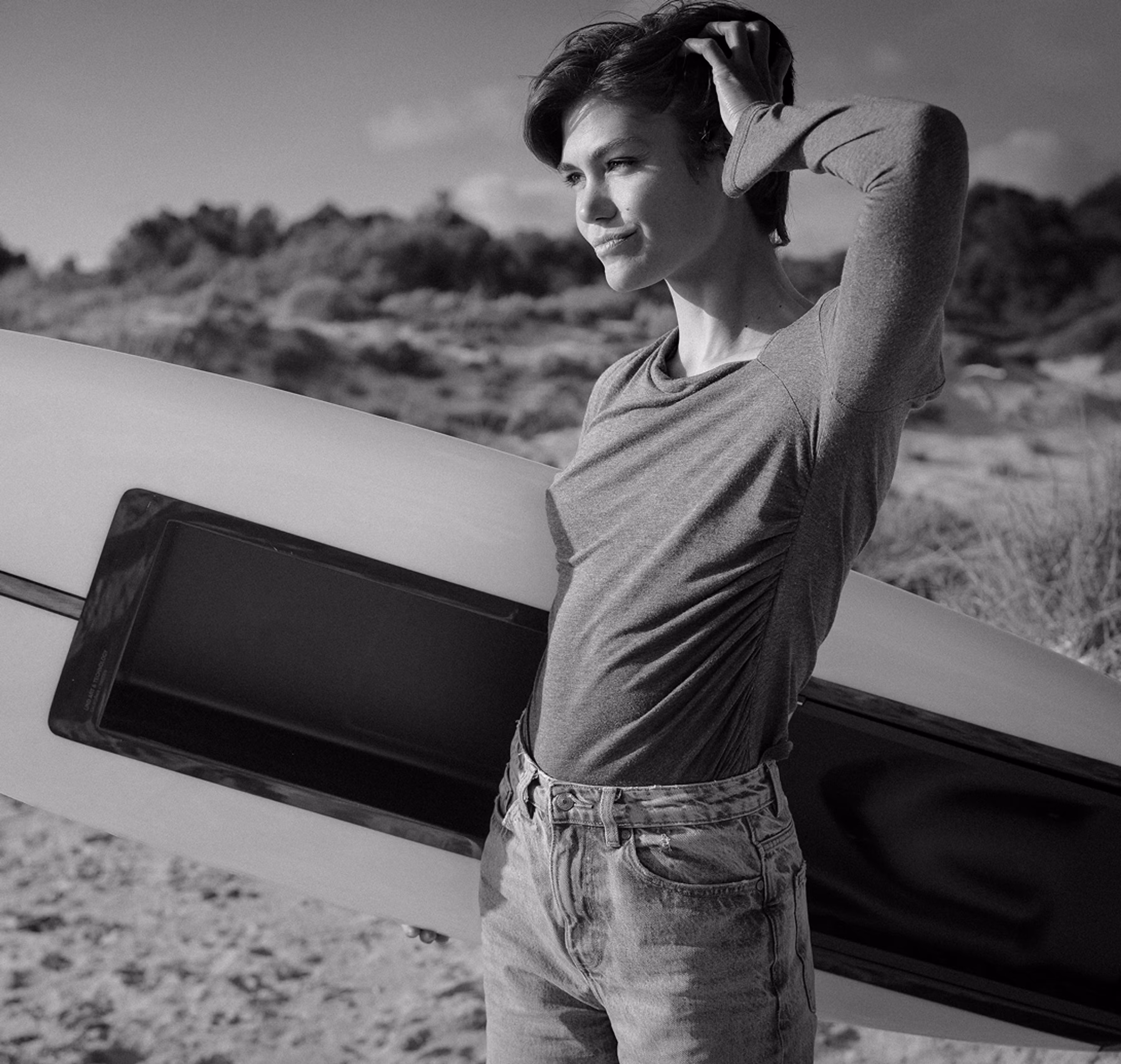 Woman posing next to a LIND electric surfboard on a sandy beach