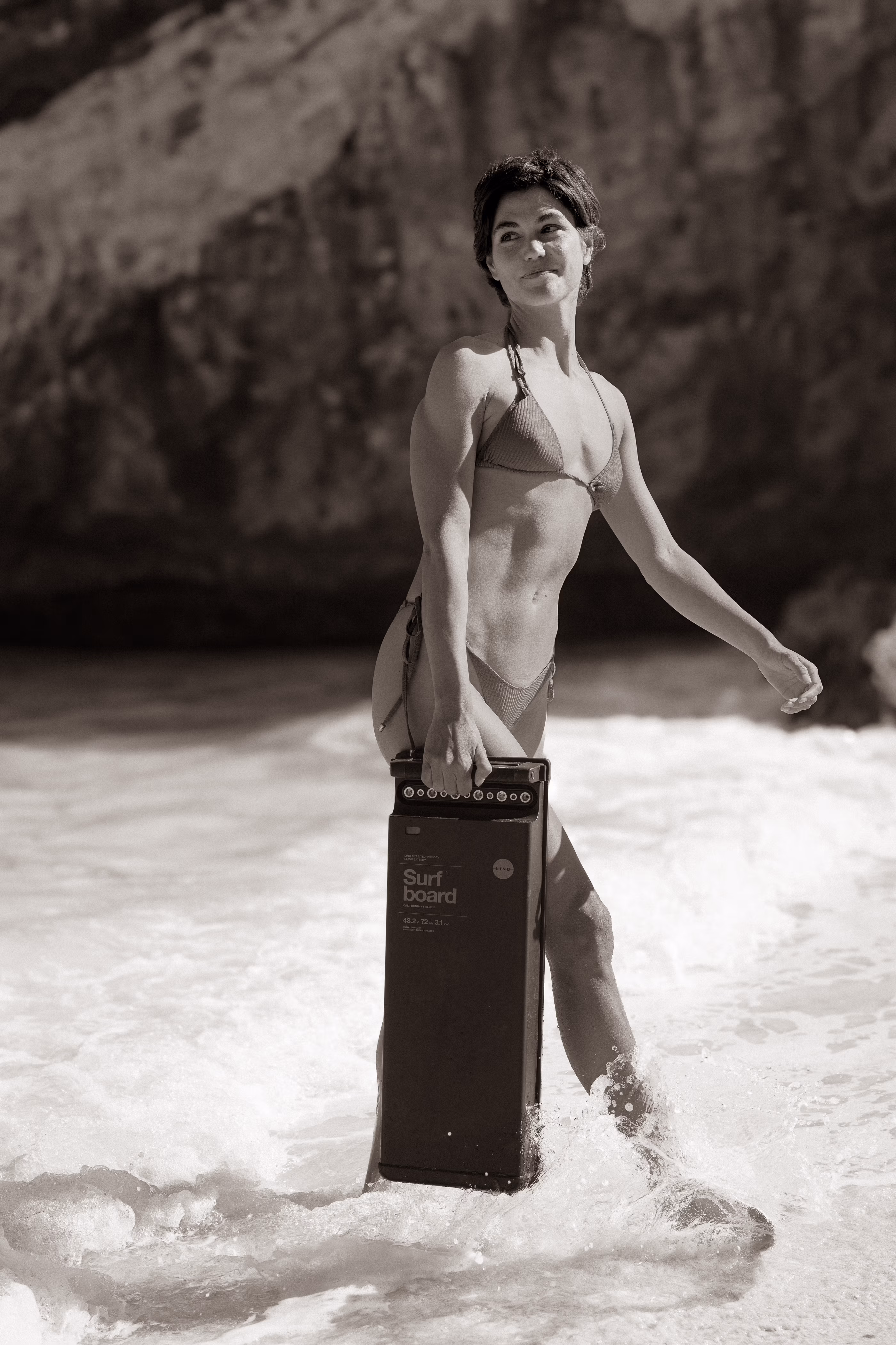 Woman in bikini carrying the LIND electric surfboard drivetrain unit through the surf