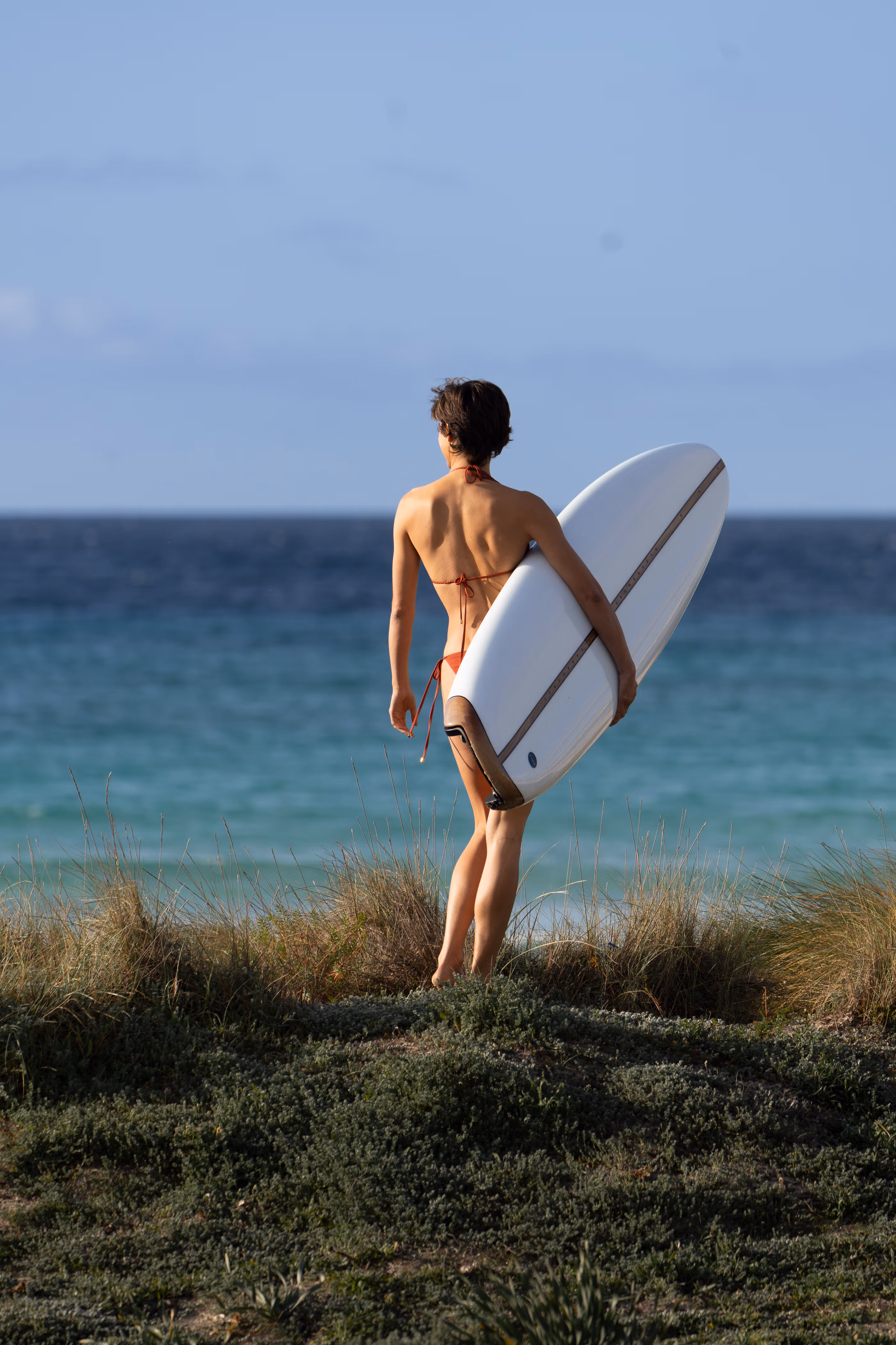 Woman in bikini carrying a LIND electric surfboard towards the ocean