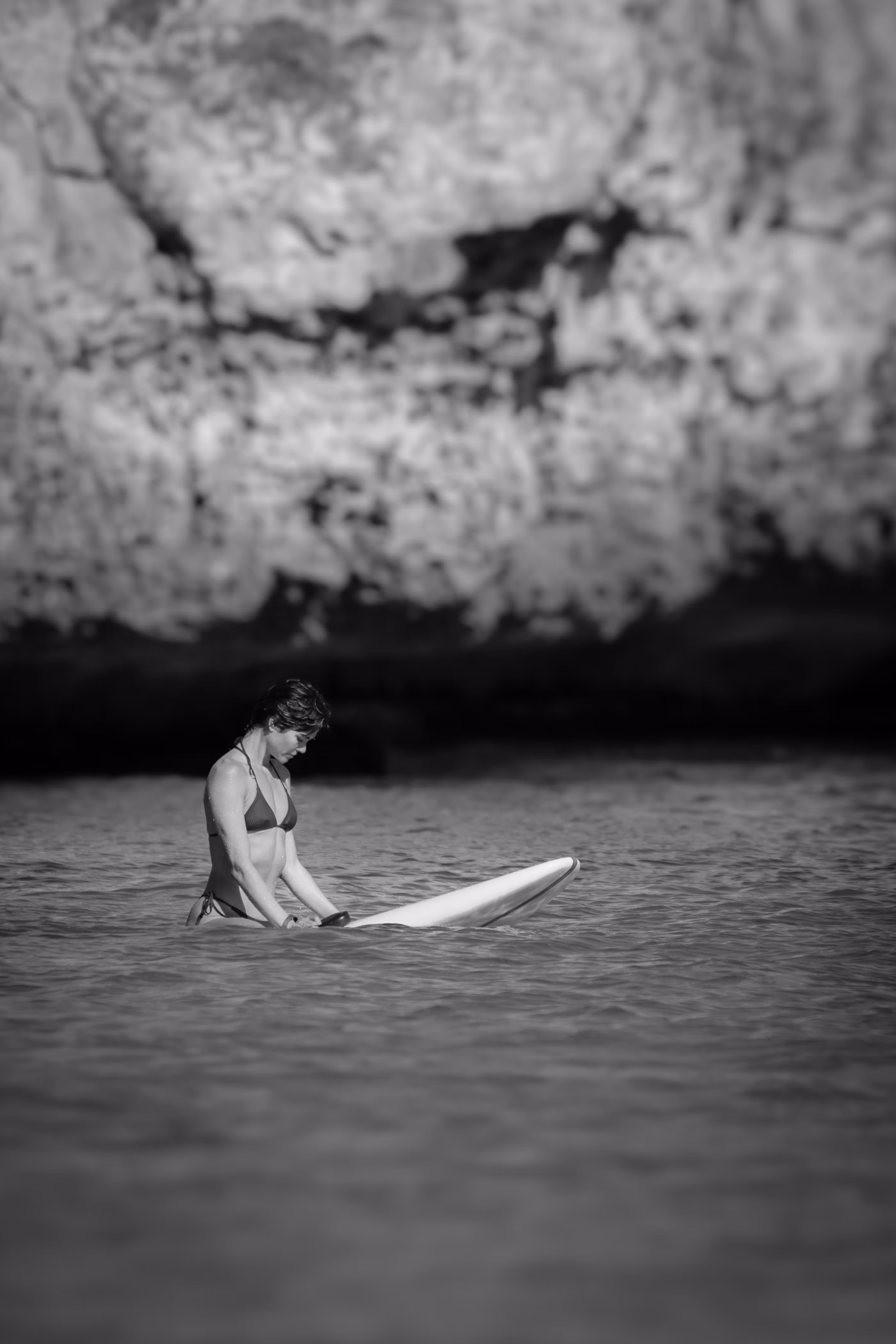 Woman in bikini preparing a LIND electric surfboard in the water by a cliff